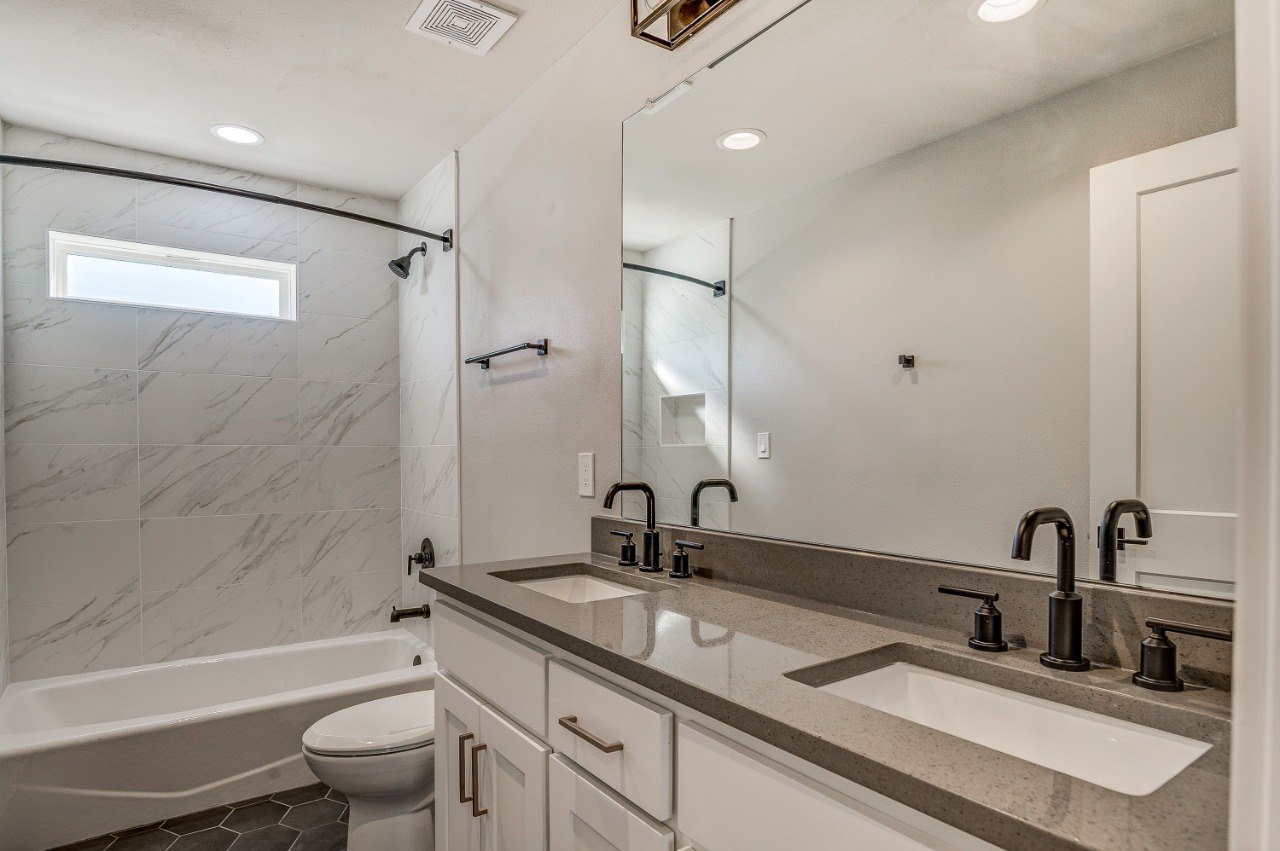 White Rock Views bathroom with a large-format marble-look tub surround, double vanity, and dark fixtures.