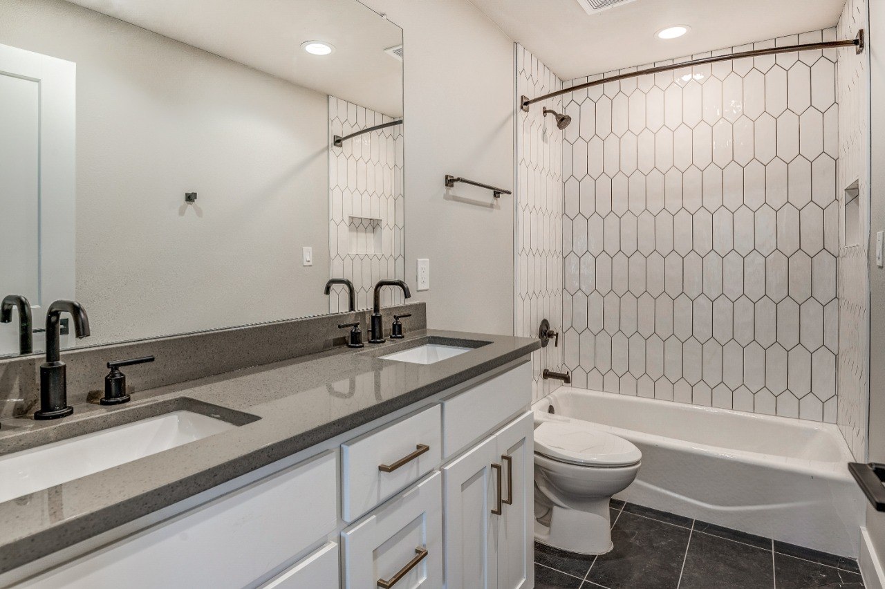White Rock Views bathroom with elongated picket tile, a tub, double vanity, and dark fixtures.